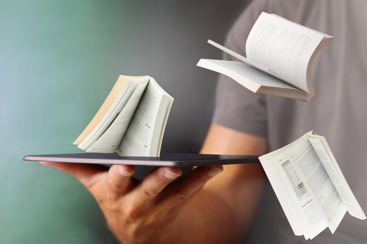 Foto van een hand die een tablet vasthoudt als een dienblad met daar op drie vallende boeken.