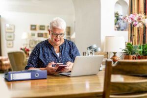 Vrouw zit thuis achter haar laptop en scant met haar mobiel de DigiD-code